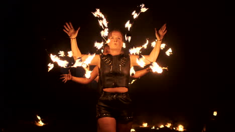 Three-women-with-burning-hoops-dance-with-fiery-torches-in-leather-clothes-in-a-dark-hangar-demonstrating-a-circus-fire-show-in-slow-motion